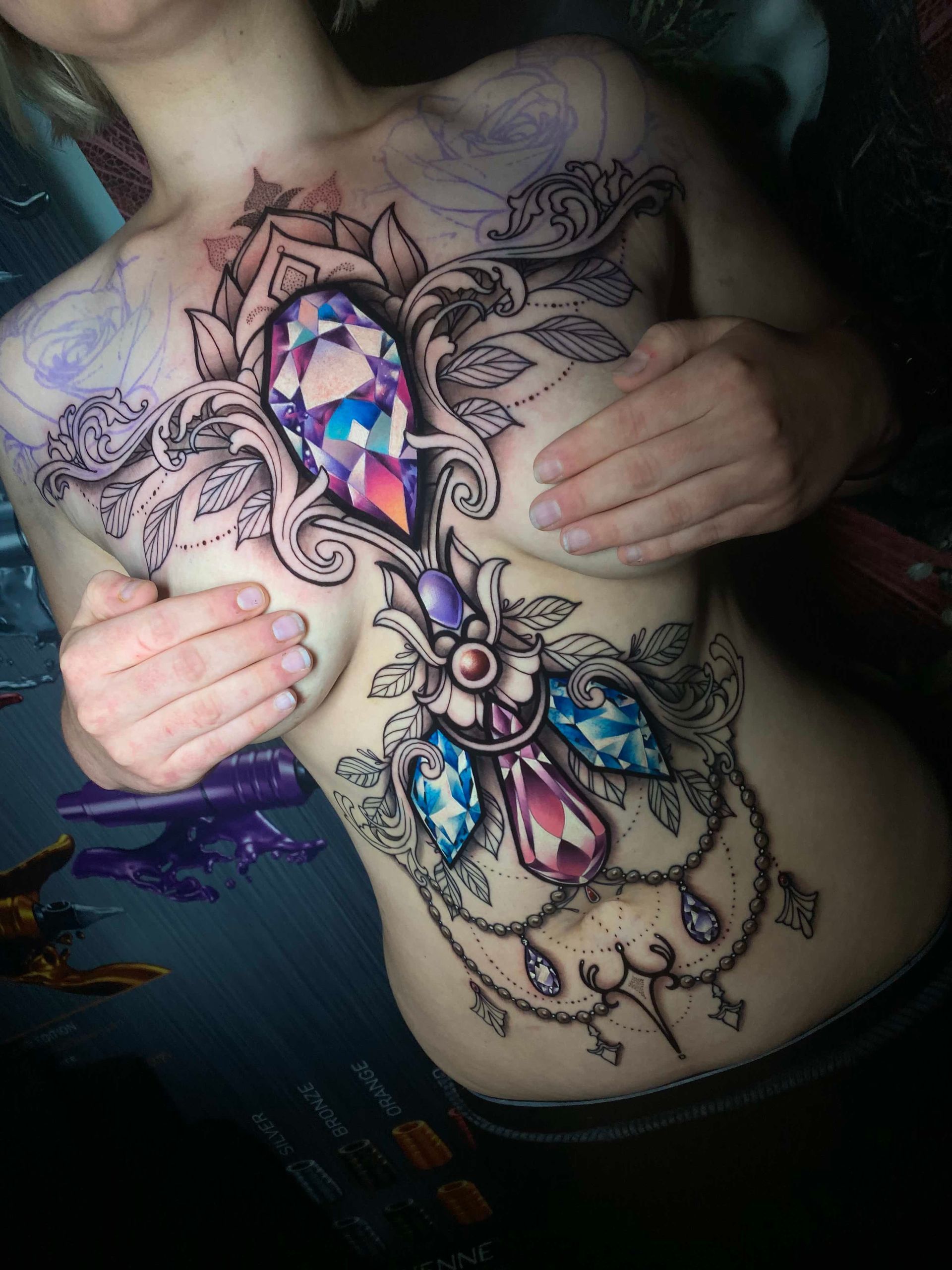 Woman with gemstone tattoo on chest, hands covering breasts.