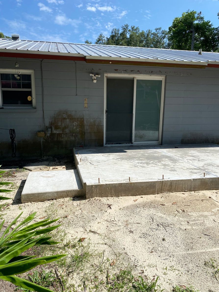 A concrete patio with a step and sliding door. Gray house with a metal roof.