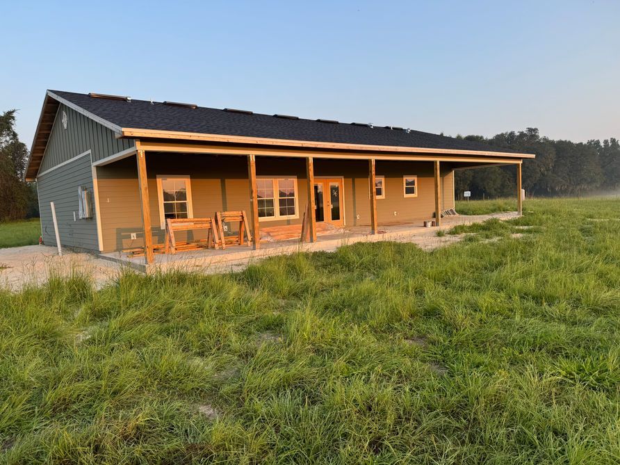 Newly built, one-story house with porch, gray siding, black roof, set in a field of green grass.