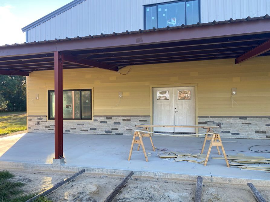 Building exterior with covered patio, tan siding, stone accent, concrete, metal beams.