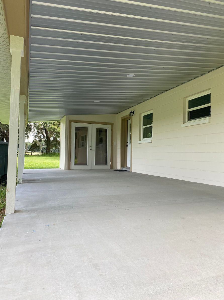 Covered porch with concrete floor, white siding, and French doors. Green lawn in the background.