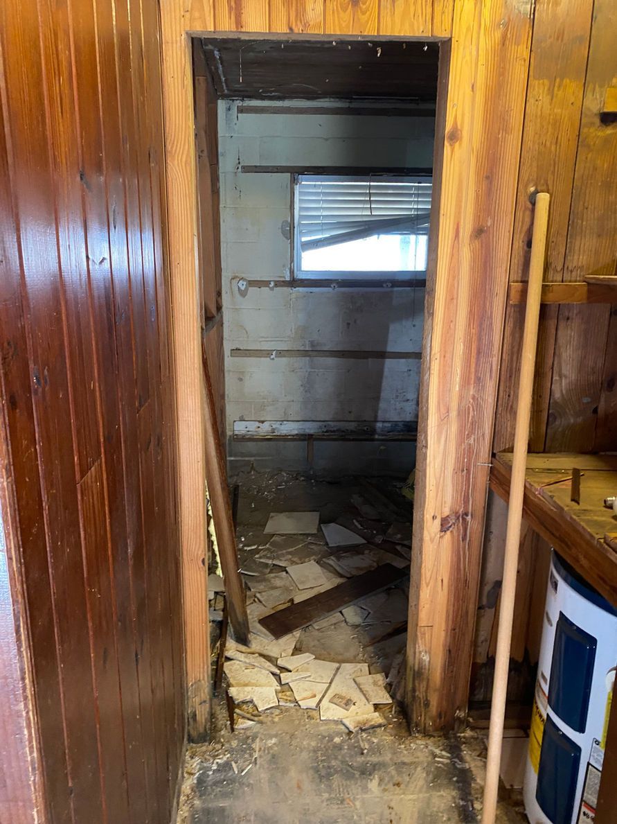 An unkempt doorway leads to a small, messy room. Wood paneling and exposed beams are visible.