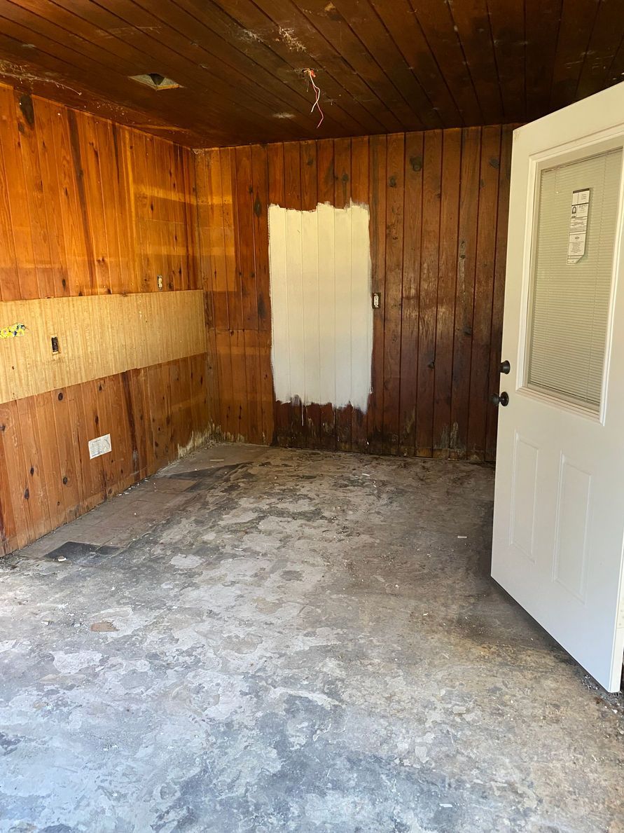 An empty room with peeling wood walls and a white door.
