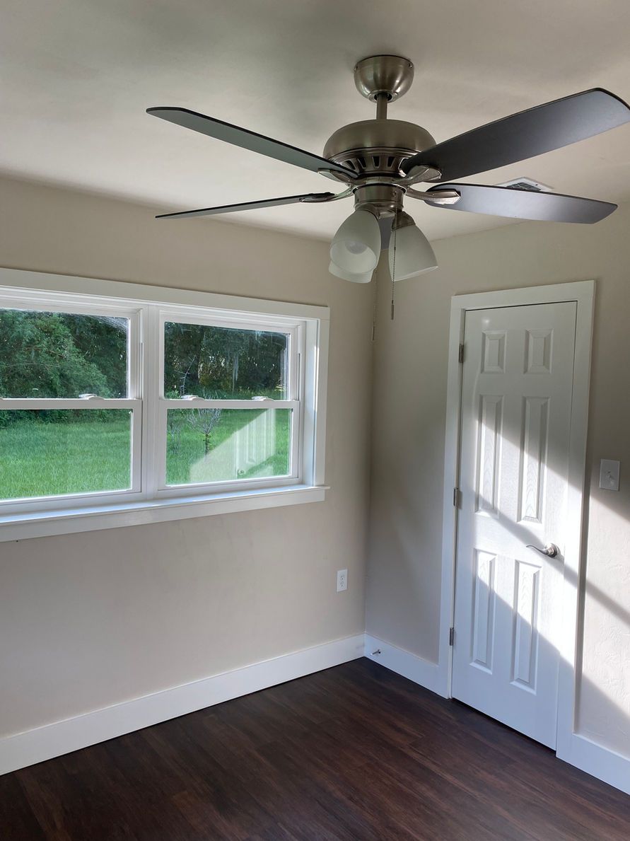 Empty room with window, white trim, ceiling fan, and dark wood floor.