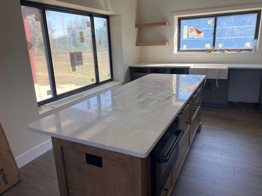 Kitchen island with white countertop and wood cabinets, near windows.