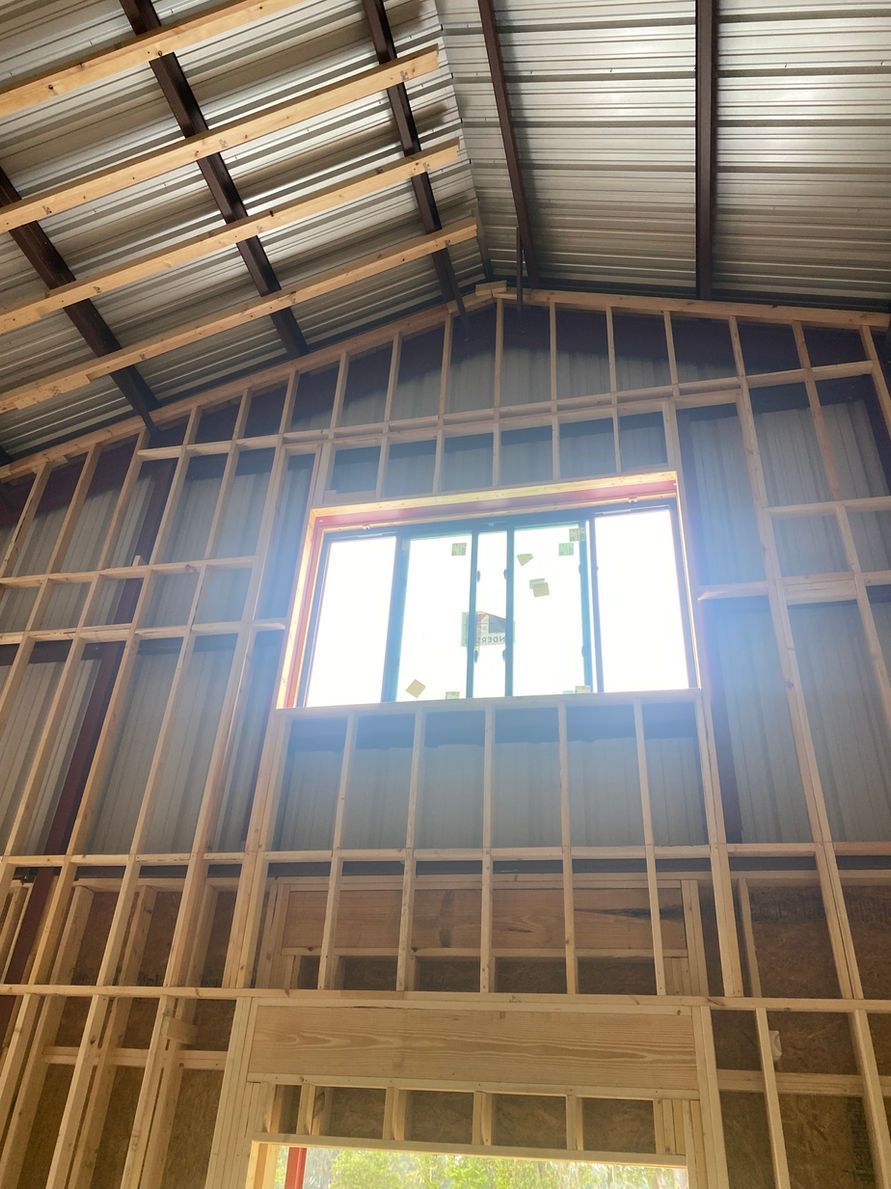 Interior view of a partially framed building. Wooden studs create walls around a window with a metal roof overhead.