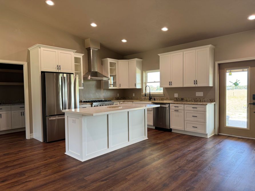 Bright white kitchen with stainless steel appliances, island, and wooden floors.