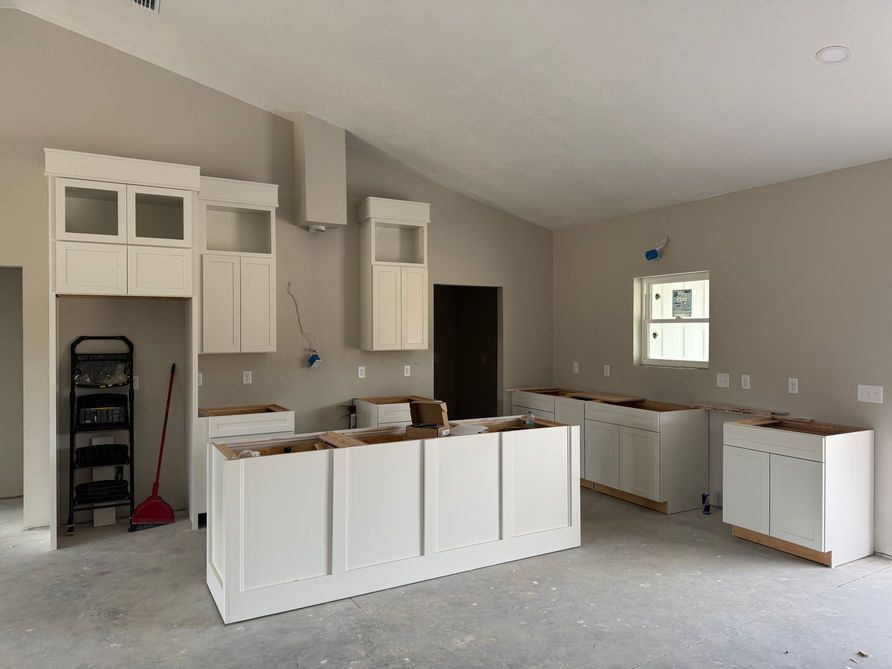Kitchen under construction with white cabinets, island, and neutral walls; window and door visible.