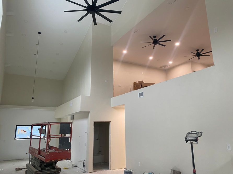 Interior view of a room with high ceilings, a loft, ceiling fans, and construction equipment. White walls.