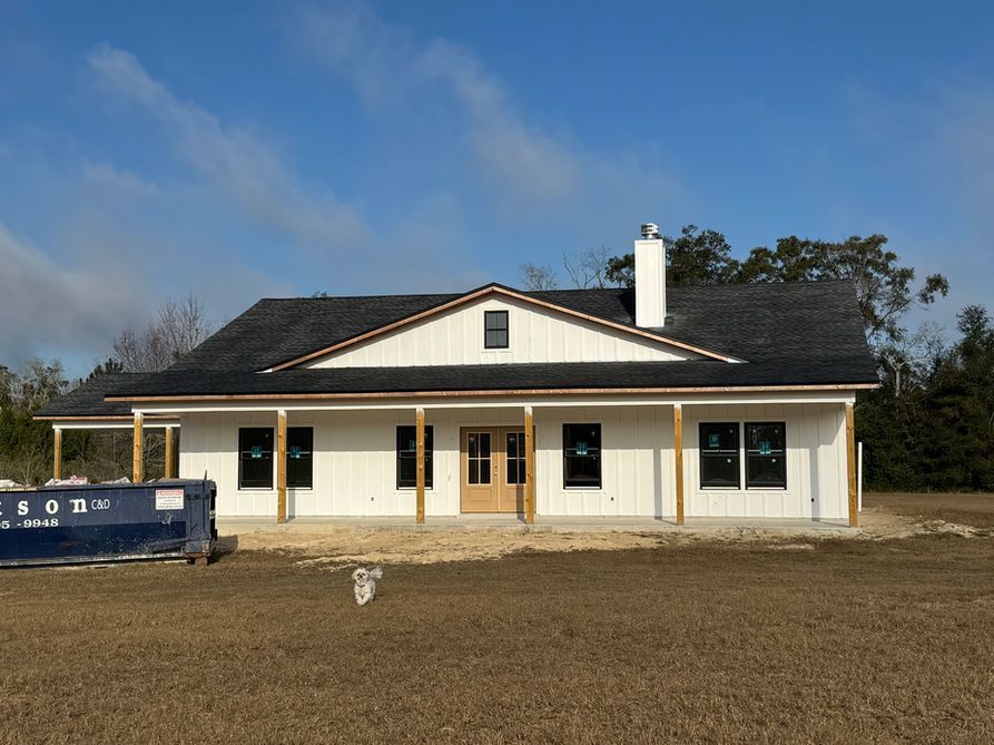 White farmhouse under construction with black-framed windows and a wooden porch.