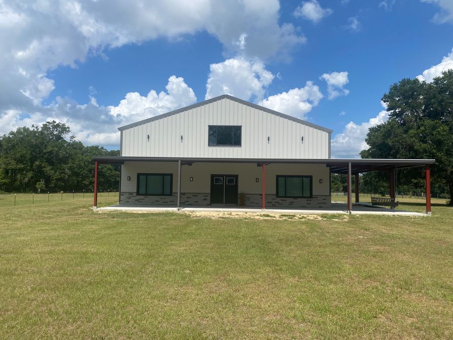 Metal building with a porch on a grassy field, under a blue sky with puffy clouds.