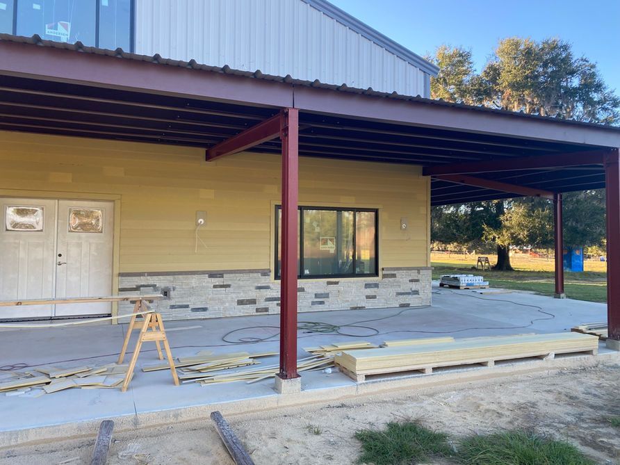 Construction of a building with a tan exterior, stone accents, and a covered porch supported by burgundy beams.