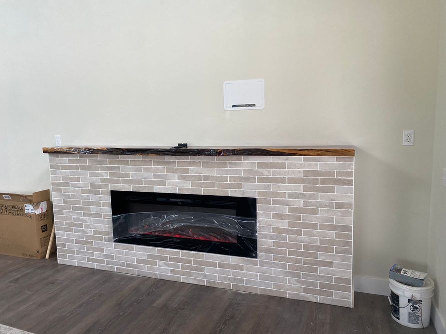 Fireplace with brick surround, wooden mantel, and an electric fireplace insert. Beige and brown tones.