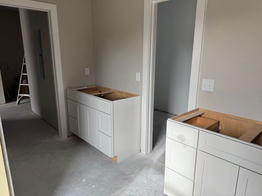 Two unfinished bathroom vanity cabinets in a room with light gray walls and doorways.