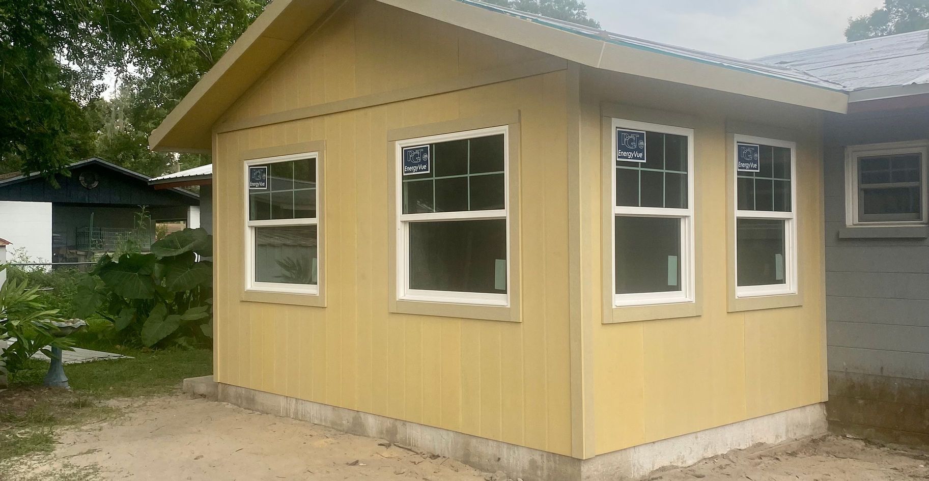Yellow-sided structure with white-framed windows, adjacent to another building; outdoor setting.