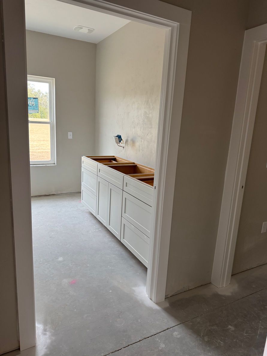 Bathroom in construction, with white cabinets, window, and unfinished walls and floor.