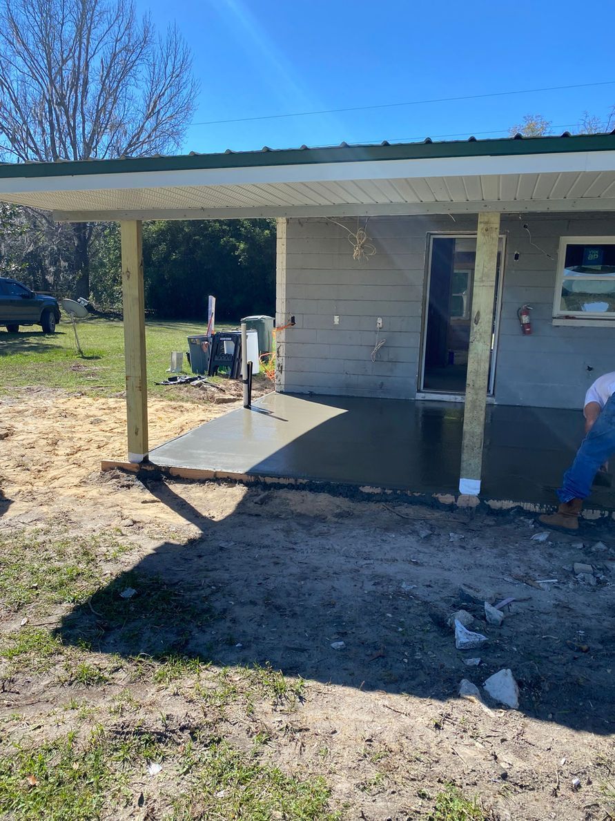 Concrete patio under a covered structure. A person stands nearby. Outdoors, sunny day.
