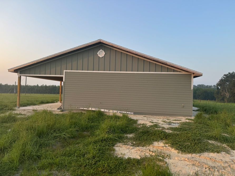 Gray barn with a covered porch in a field.