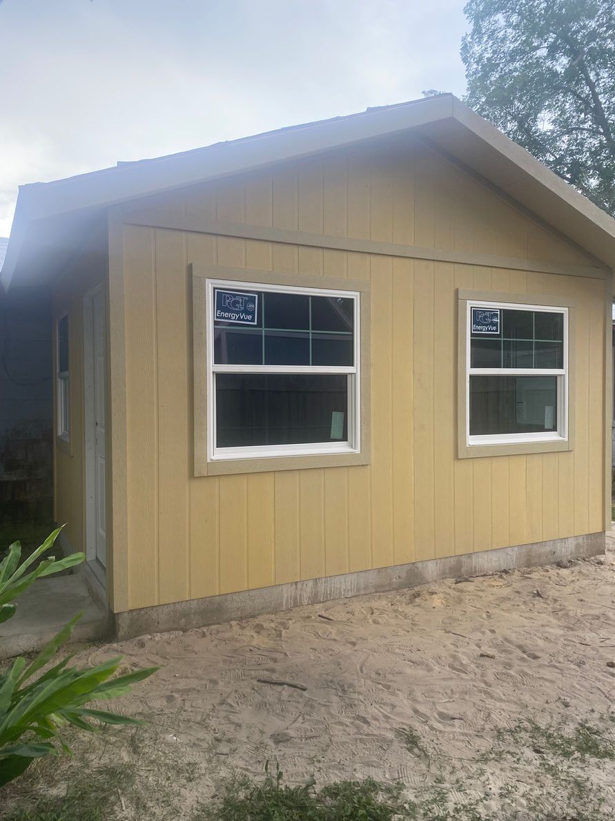 Yellow shed with two windows and a door on a gravel lot.