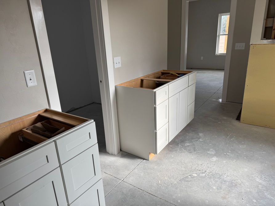 Unfinished white kitchen cabinets in a room with concrete flooring, doorway, and neutral walls.