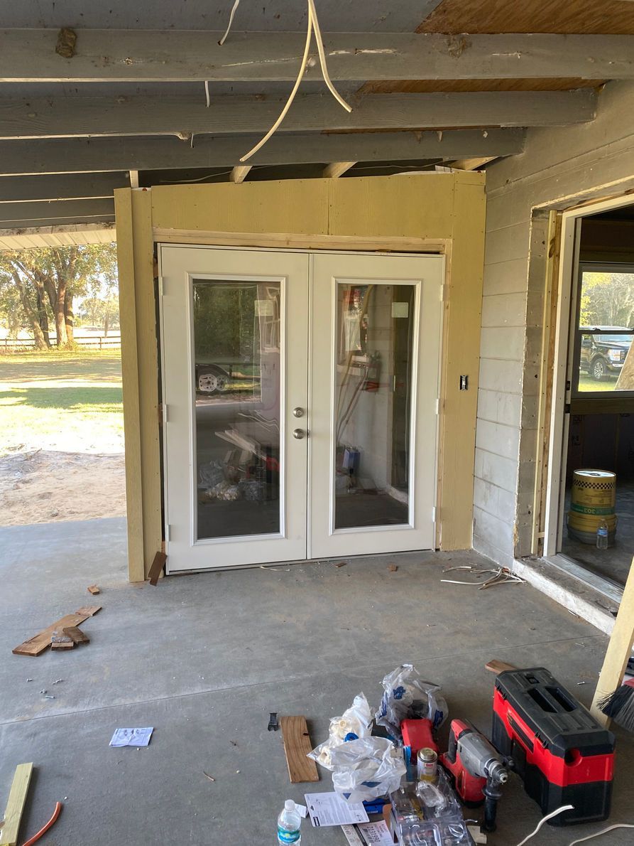 French doors set into a porch under construction; tools and debris are visible.