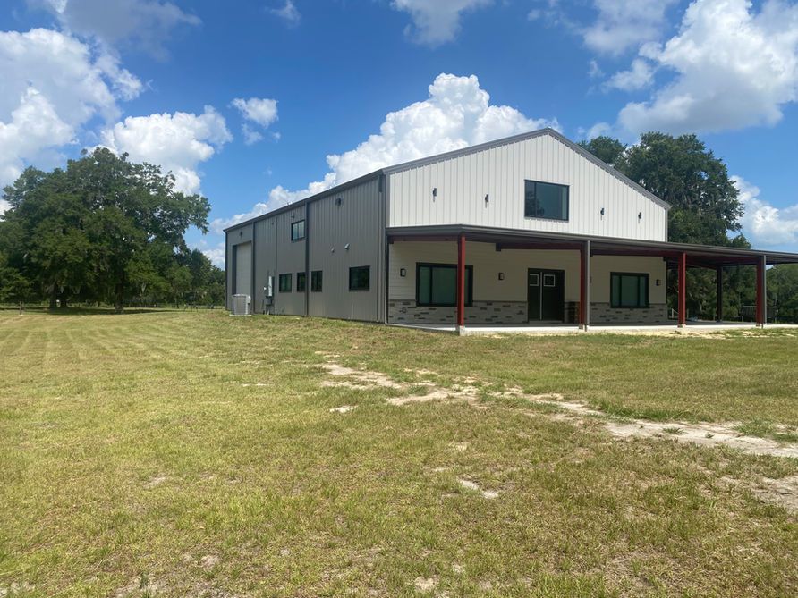 A metal building with a covered porch on a grassy field under a blue sky.