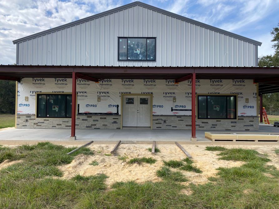 A partially constructed metal building with a stone facade and a porch under a blue sky.
