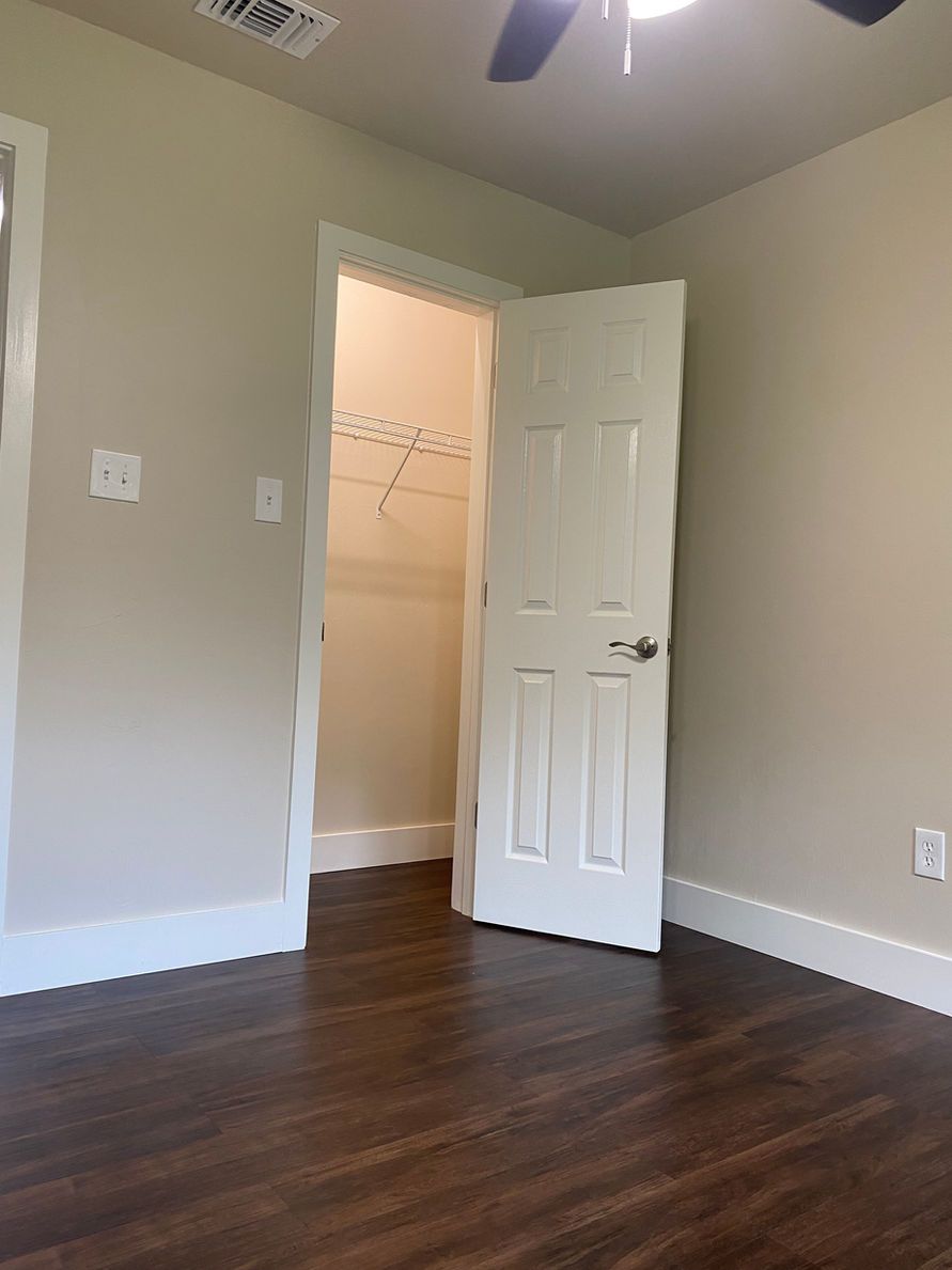 Bedroom with open closet door, dark wood floors, and white trim.
