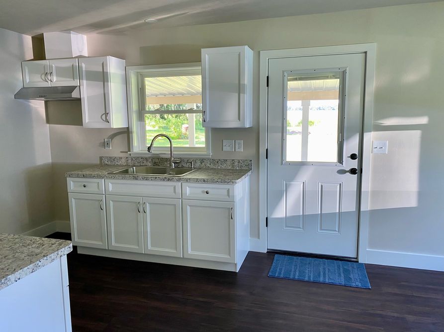 Kitchen with white cabinets, granite countertop, window, and door. Dark wood floor.