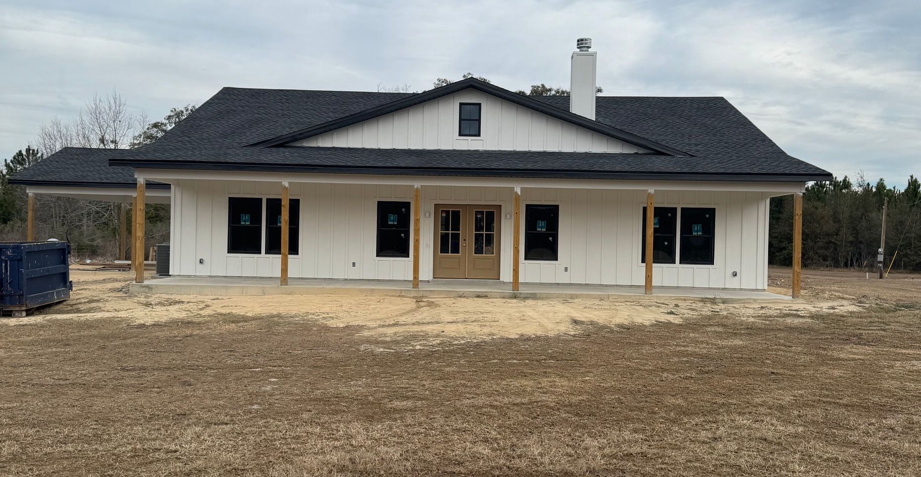 White farmhouse under construction with black roof, wooden supports, and a chimney.