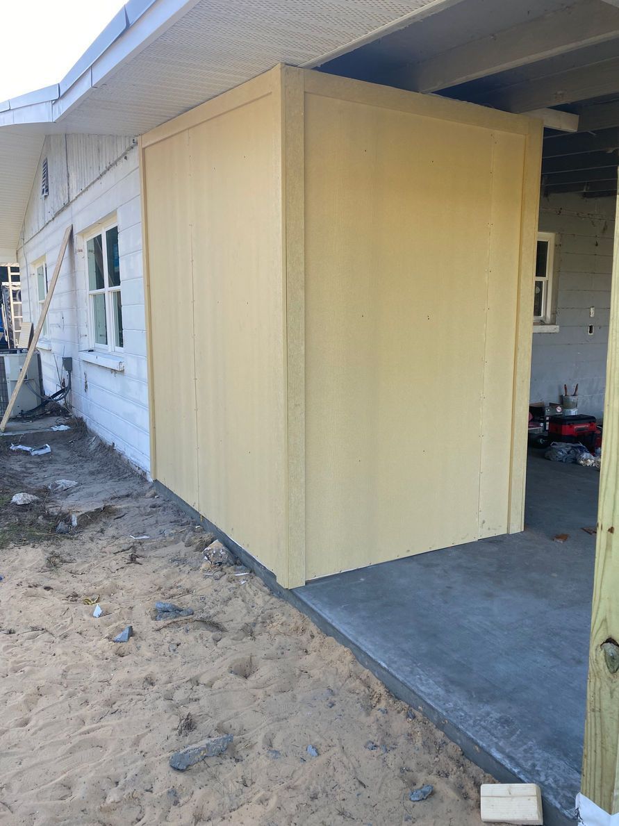 Exterior view of a building with a newly constructed, yellow-sided structure. Sand and concrete are visible.
