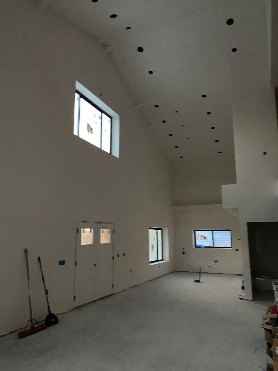Interior of a room with white walls, recessed lights, and windows. Unfinished with tools visible.