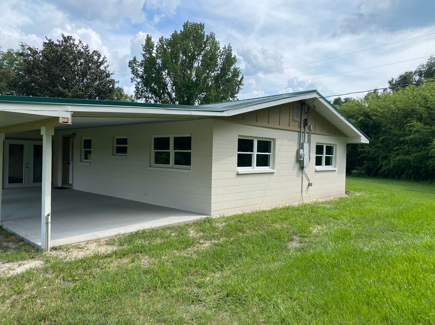 White brick house with green roof, porch, and windows on a grassy lot.