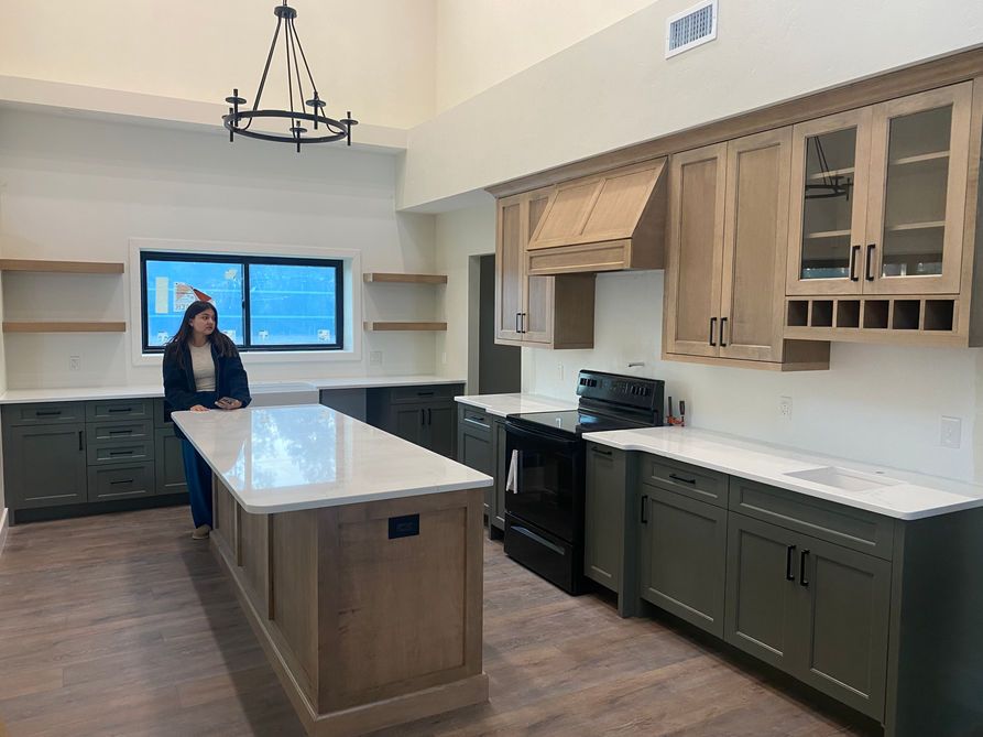 A woman in a kitchen with green and light-colored cabinets and an island.