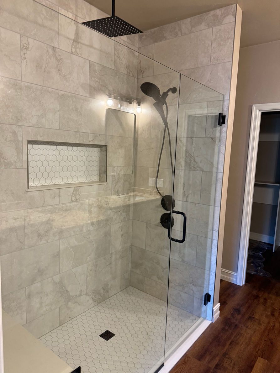 Modern glass shower with gray tiled walls, black fixtures, and white hexagon floor.