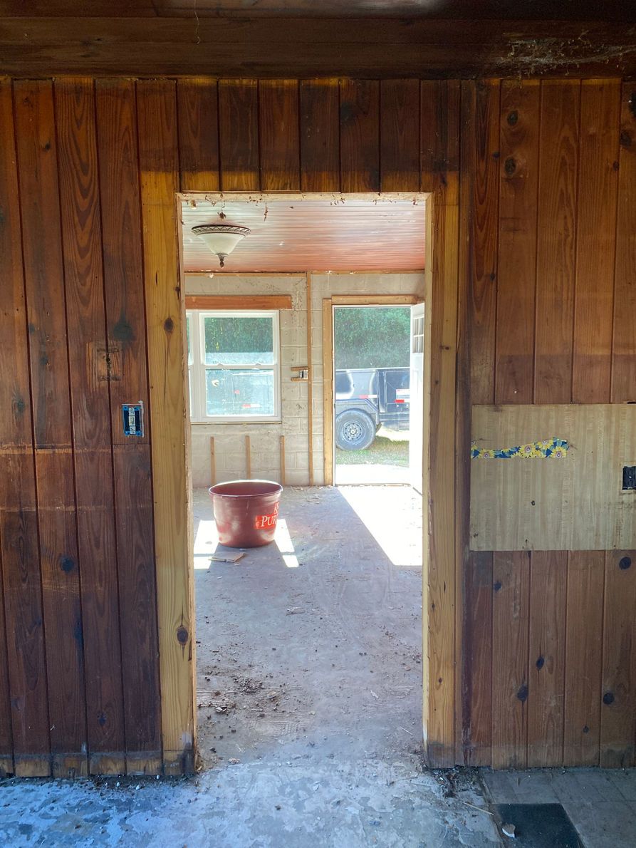 Interior view of a wooden-paneled doorway leading to a sunlit room with a window, revealing a vehicle.