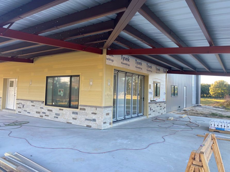 Construction site: covered patio with stonework, yellow siding, metal roof, and folding glass doors.