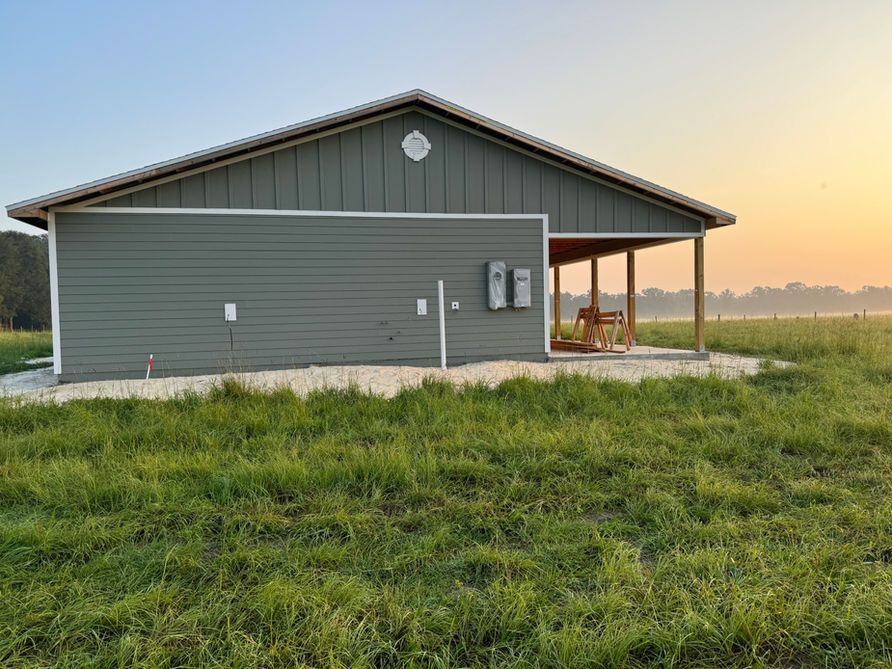 Green building with covered porch in a grassy field at sunrise.