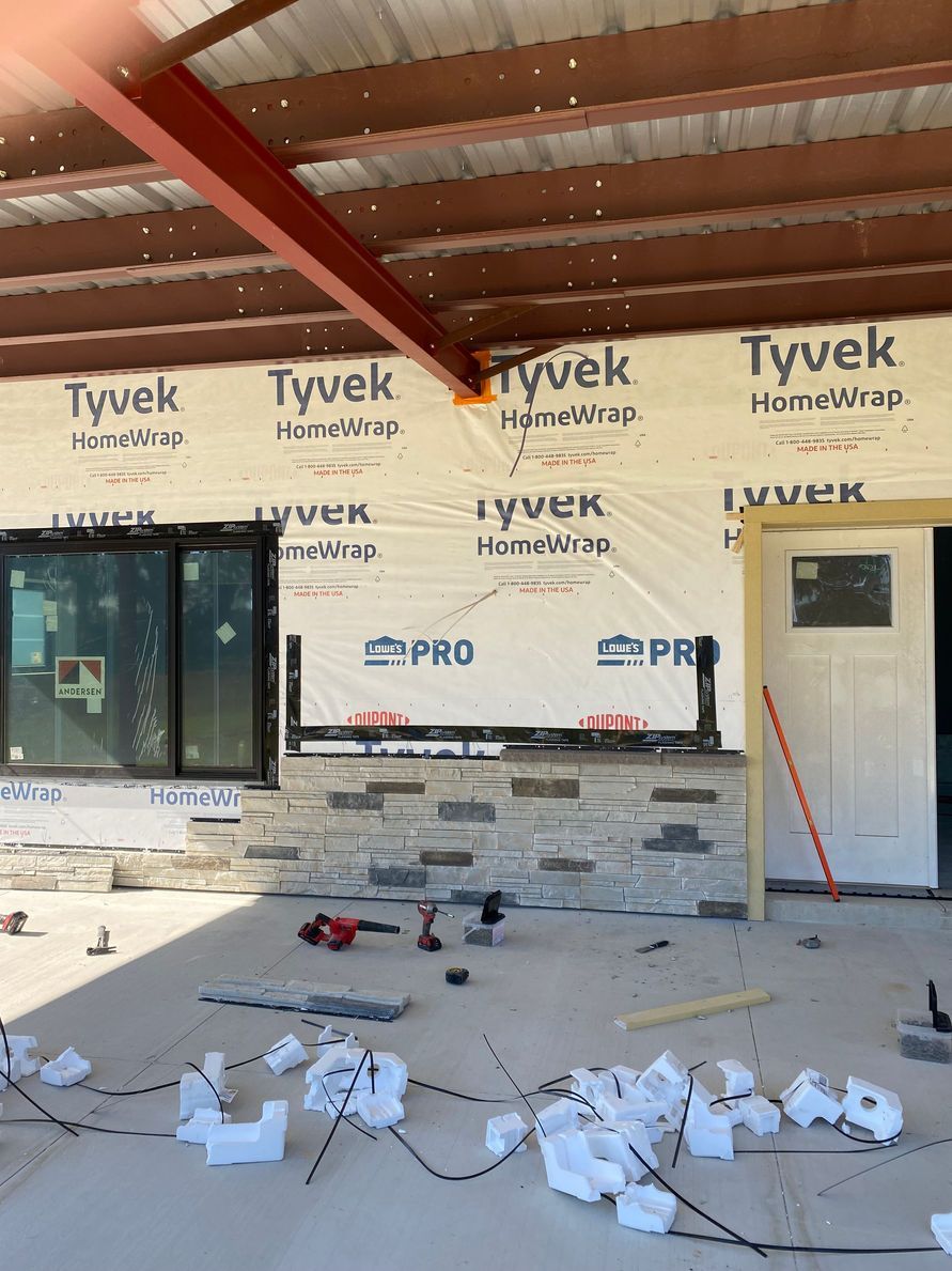 Construction site with stone veneer, window, door, Tyvek wrap, and red beam.