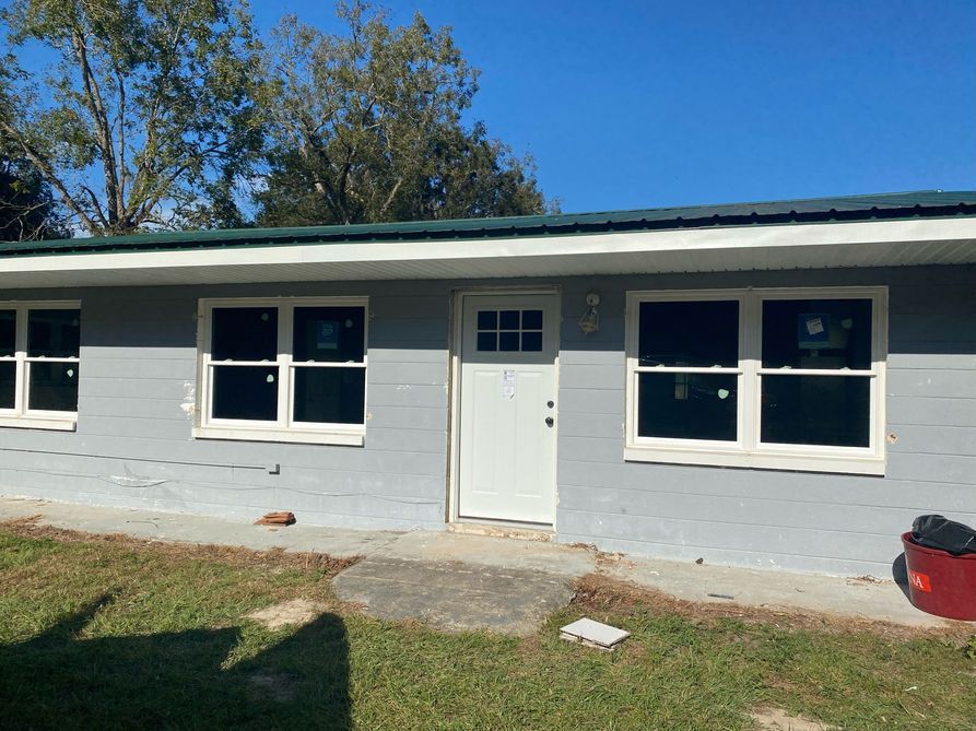 A one-story building with white framed windows and door, gray siding, and a green roof.