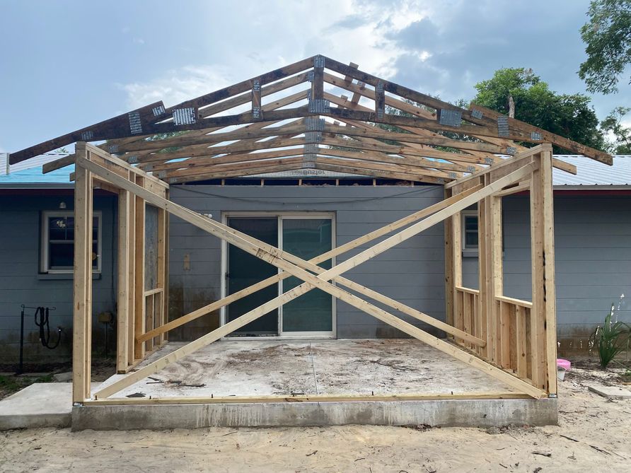 Wooden frame of a porch being built against a house with a sliding glass door; grey siding.