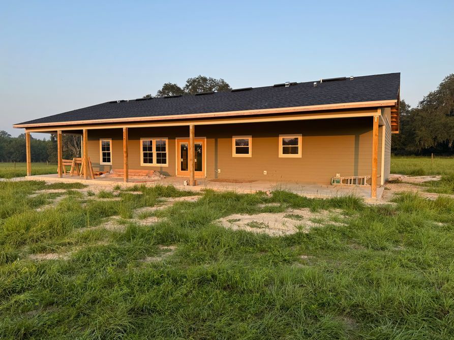 A one-story house under construction with a porch in a grassy field.