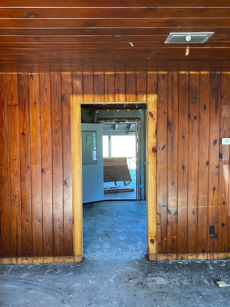 Wooden paneled interior with doorway leading to a sunlit room with a partially open door.