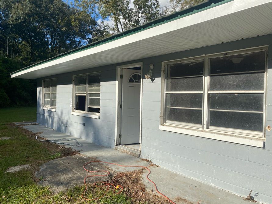 Gray house with white trim, open door, and multiple windows on a sunny day.