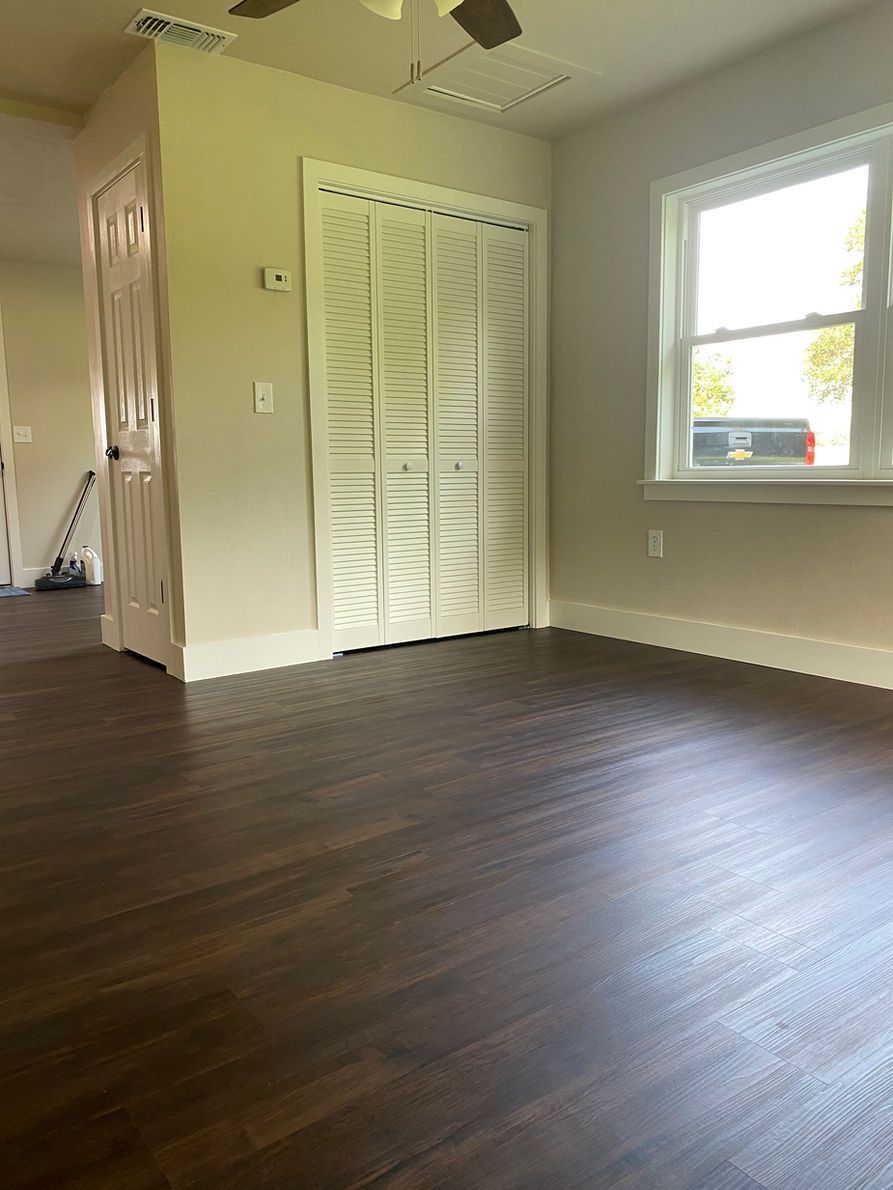 Empty room with dark wood floor, white closet doors, and a window.