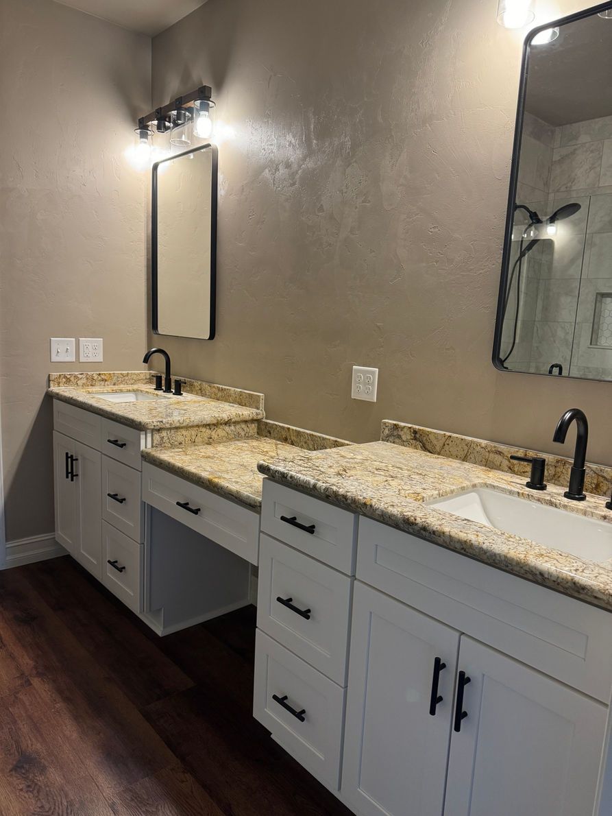 Bathroom with two white vanities, beige countertops, black fixtures, and brown floors.