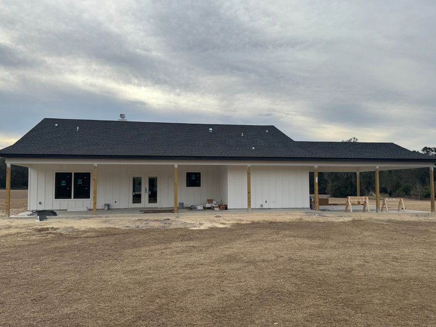 White house under construction with black roof and covered porch on a cloudy day.