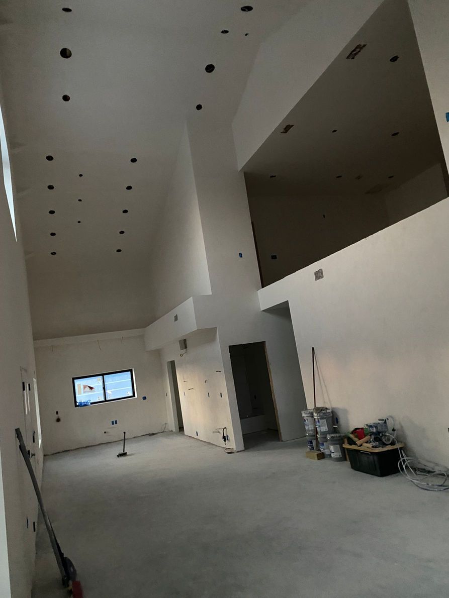 Interior of a room under construction with high ceilings, light walls, and recessed lighting.