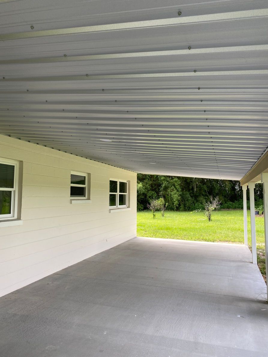 Covered patio with gray concrete floor, white walls and roof, and grassy backyard.