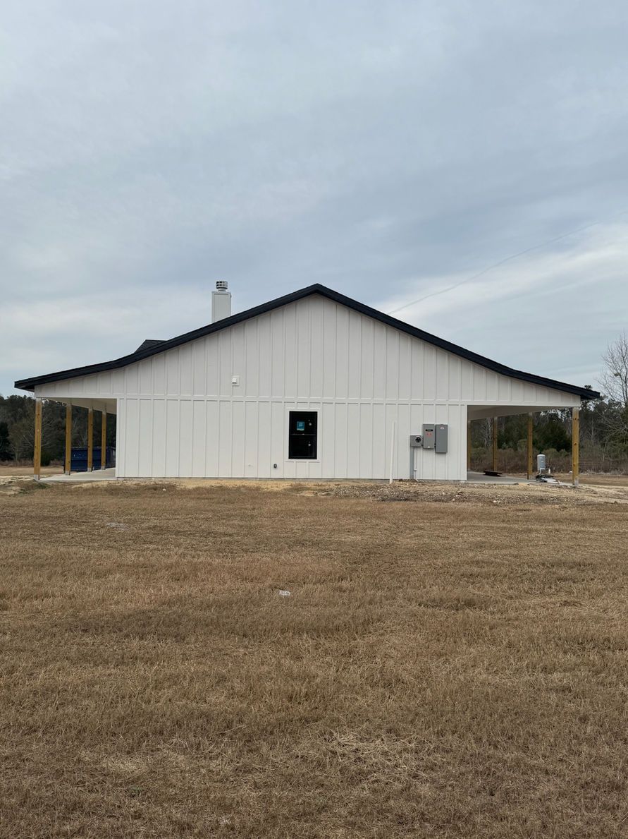 White house with black roof and porch overhangs in a field.